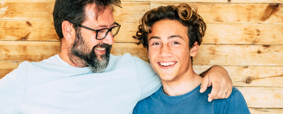 A teen son and his father arm-in-arm and smiling
