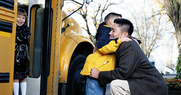 Child hugging dad by the school bus