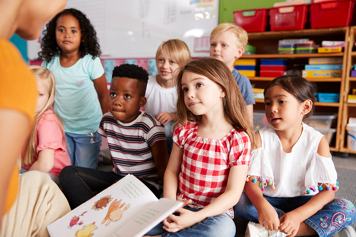  A group of students sit on the floor in a classroom listening to their teacher read a story.