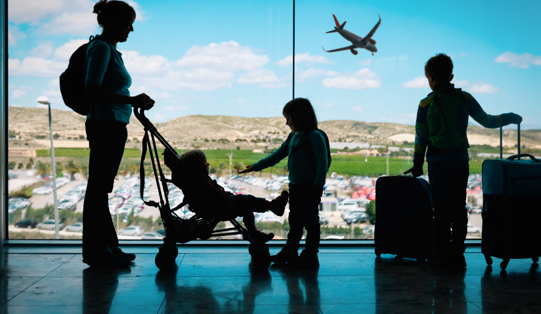 Silhouette of a family of 4 standing by the window in an airport as a plane takes off in the background.