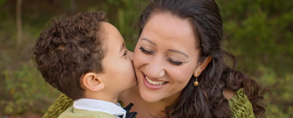 Well-dressed boy giving his smiling mother a kiss on the cheek