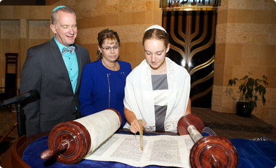 A teenage Jewish girl reads from the Torah at her Bat Mitzvah as her parents look on