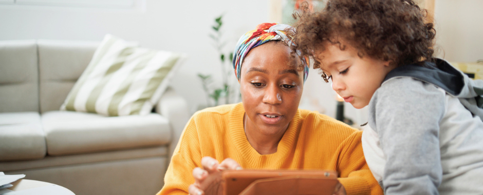 An African American mother shows her young son how to do something on an ipad