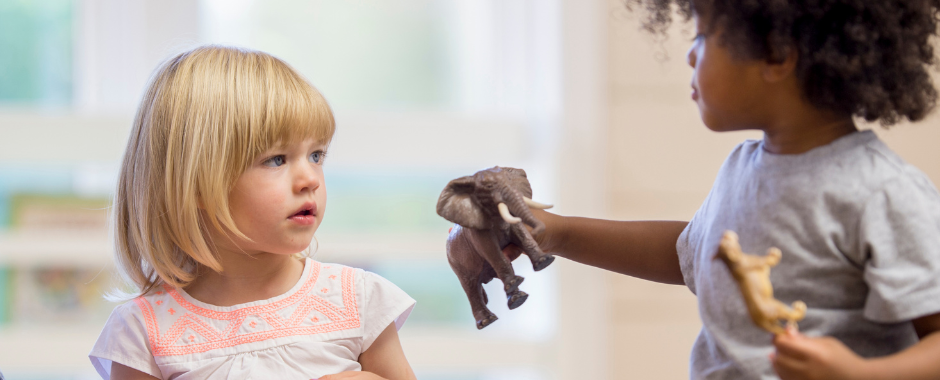 A young boy offers a toy elephant to a young girl