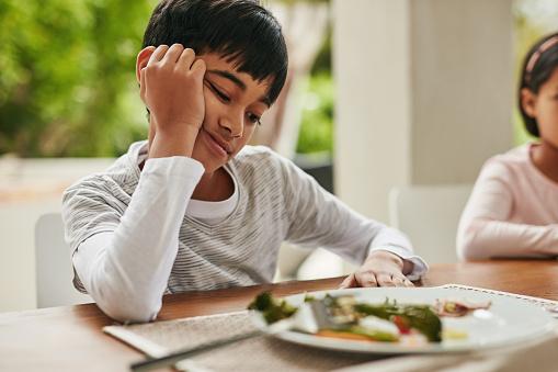 Shot of two confused looking children looking at vegetables on a plate that their parents expect them to eat while sitting around a table at home